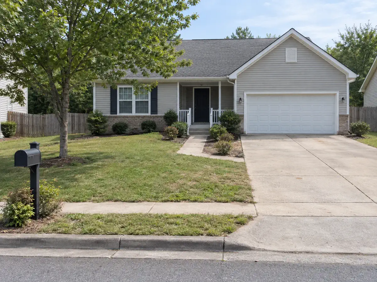 Driveway entry before AI yard design with plain lawn, sparse shrubs, mailbox, walkway, and garage access