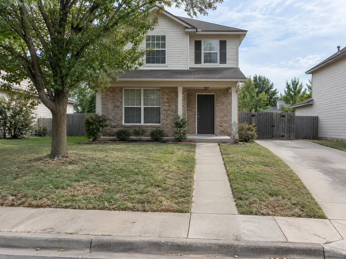 Front yard before AI yard design with a plain entry walk, driveway edge, mature tree, and sparse foundation planting